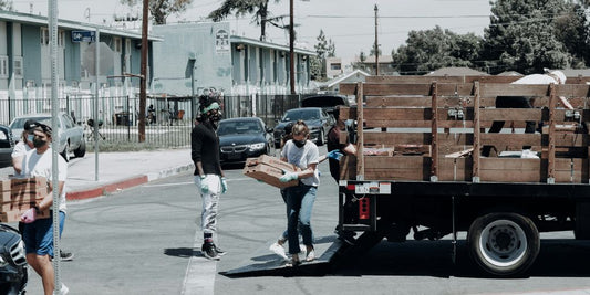 man in black jacket and blue denim jeans standing beside brown wooden box trailer during daytime